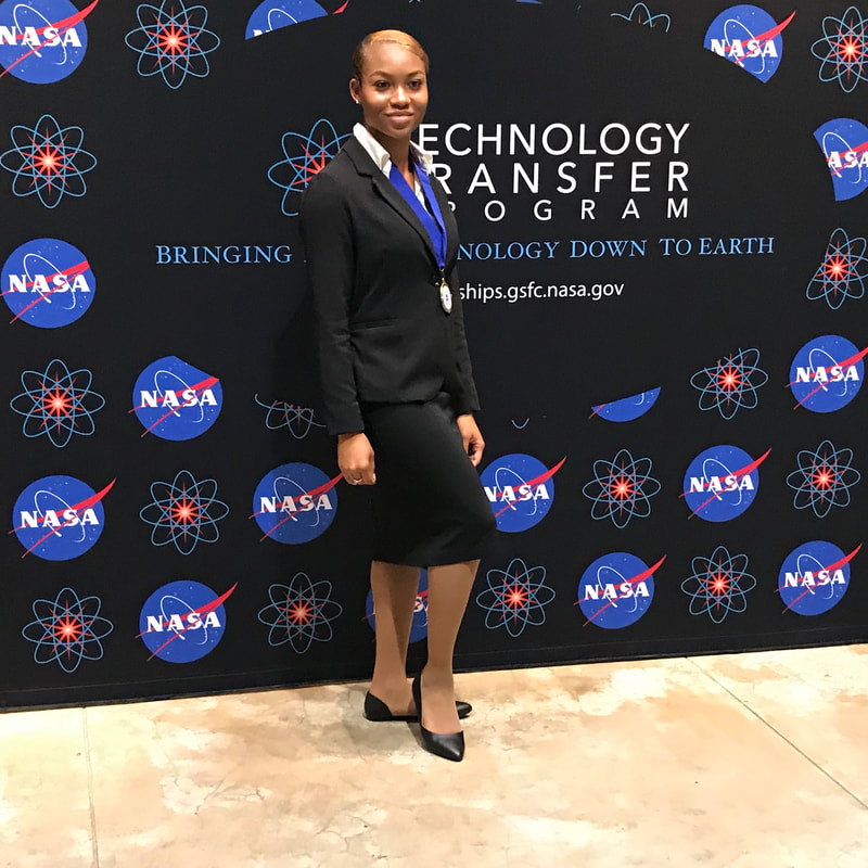 Medal recipient in a black dress posing before the NASA Technology Transfer Program backdrop