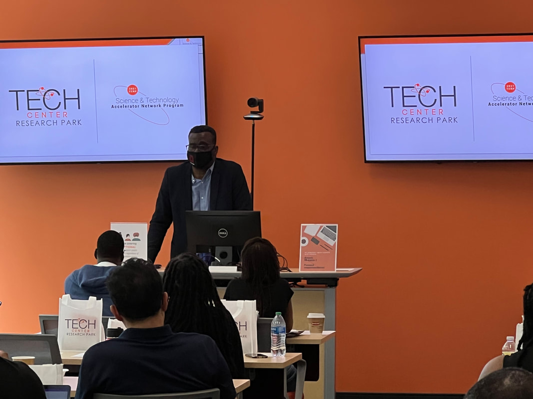 Speaker standing at the front of the room beneath Tech Center presentation screens