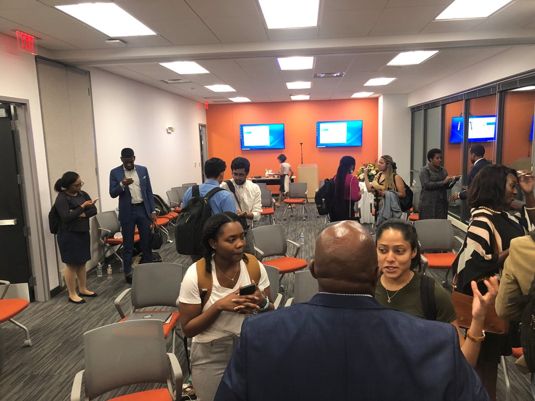 Participants mingling in a meeting room with orange walls and wall-mounted screens