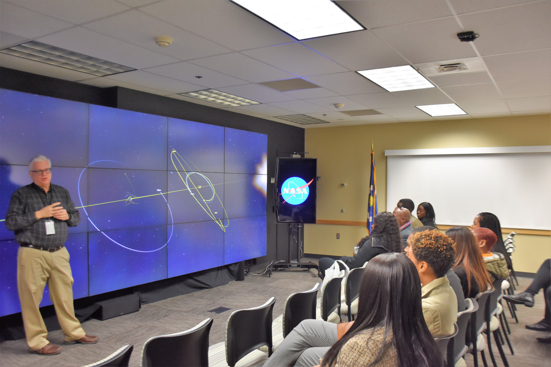 Guide explaining an aircraft display to seated visitors in a NASA exhibit room
