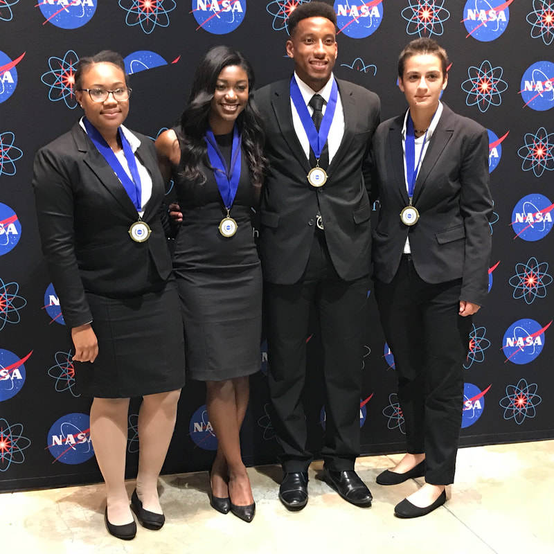 Four medal-winning team members posing together before the NASA Technology Transfer backdrop