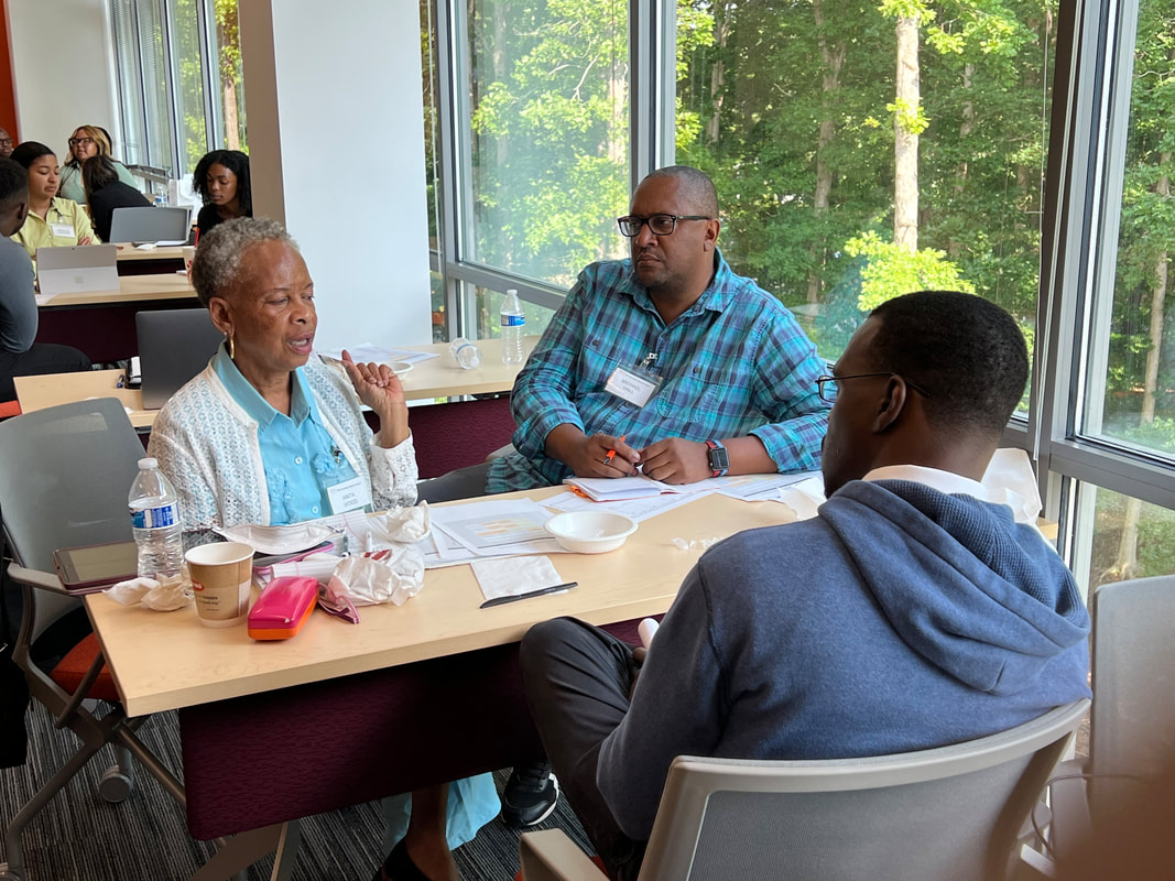 Four participants discussing ideas around a table beside large windows