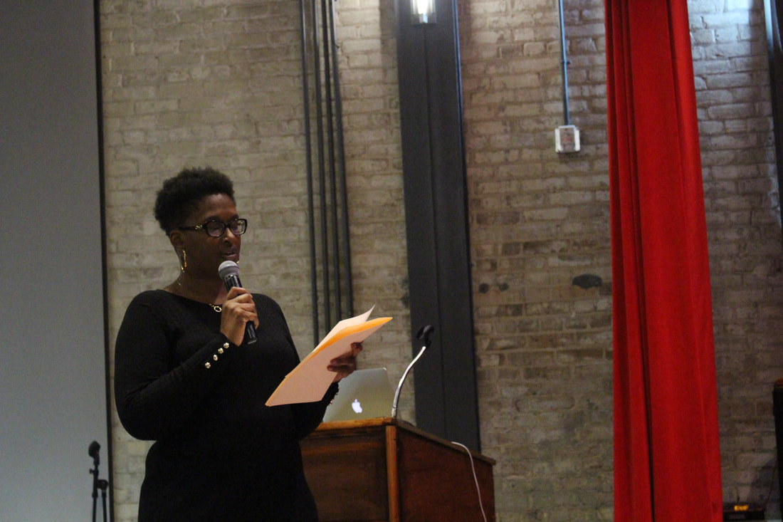 Student reading notes while speaking into a microphone beside the podium