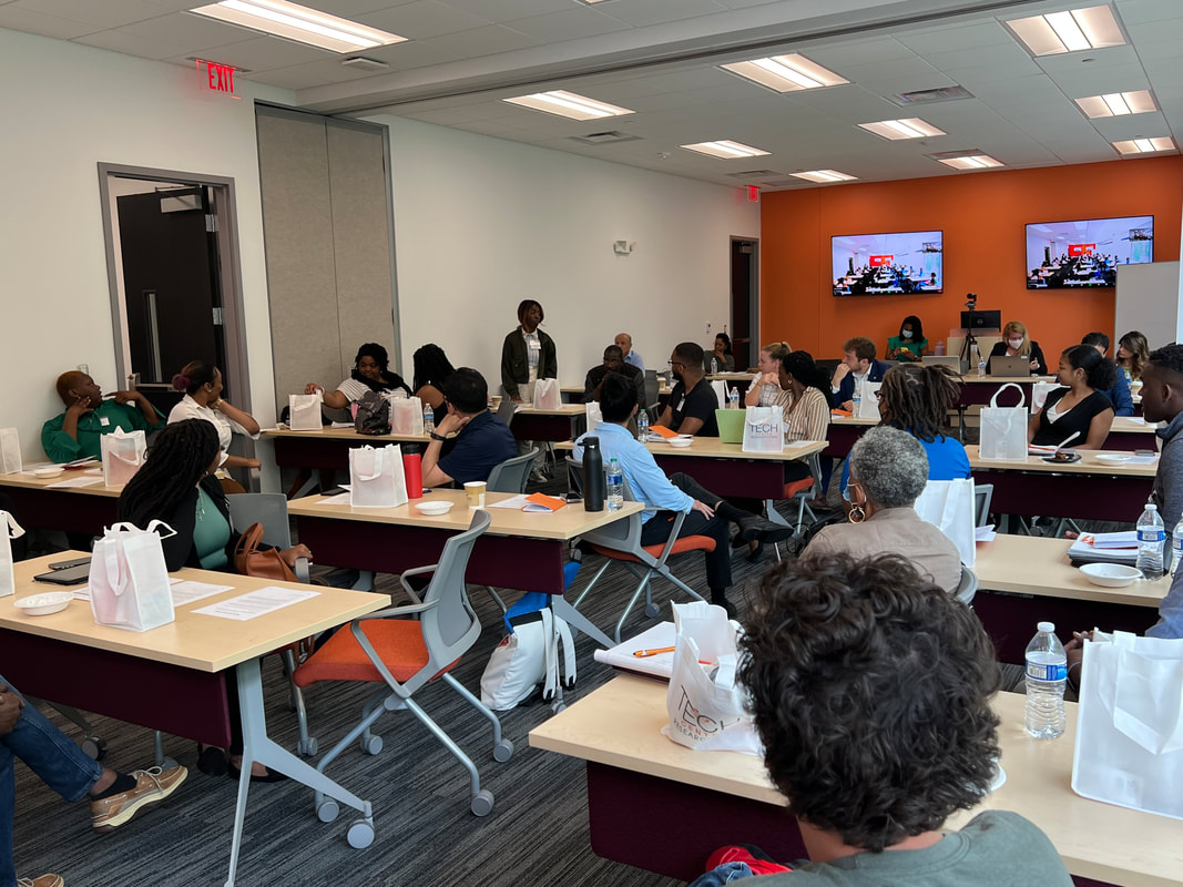 Participants listening to a discussion across several tables in the workshop room