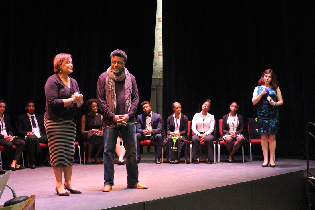 Award recipient standing with an organizer on stage while students watch