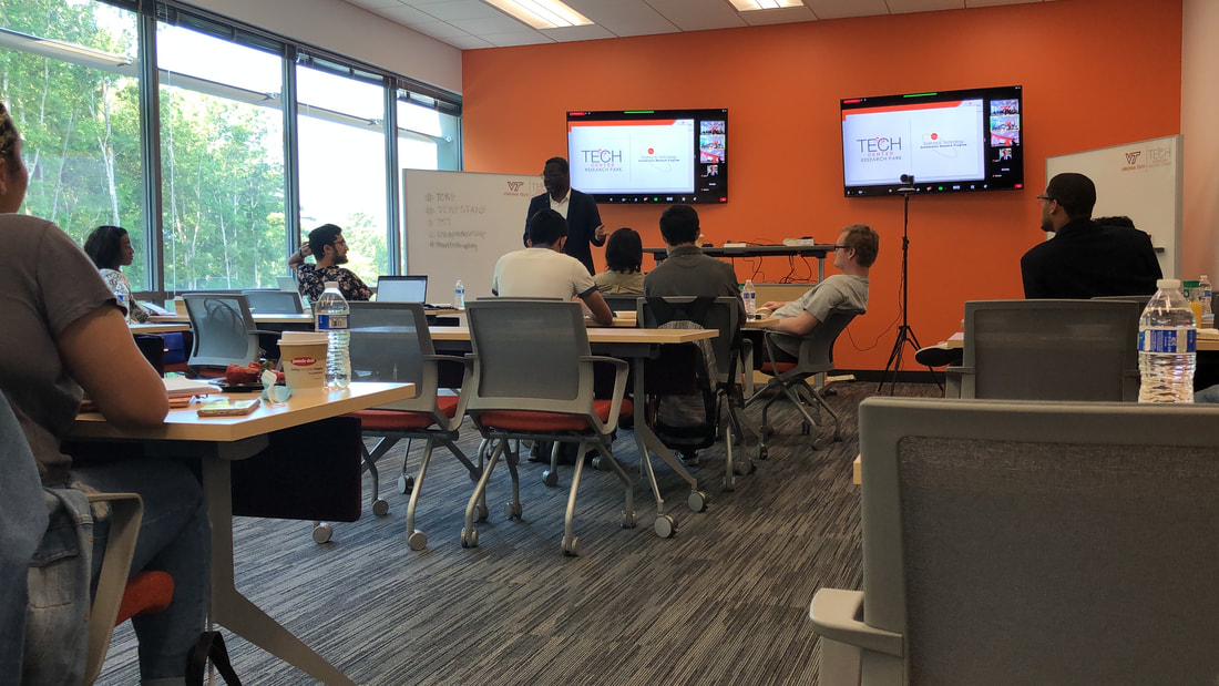 Participants listening to a presenter in the orange-walled workshop room