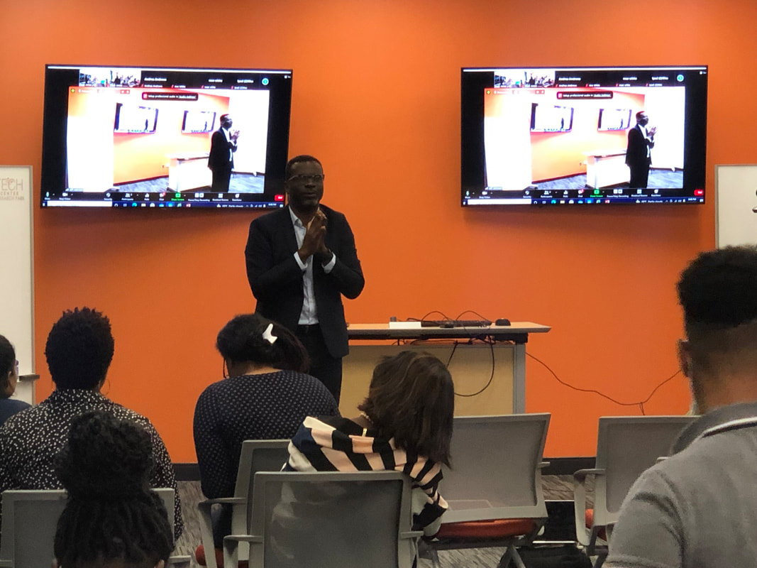 Presenter addressing workshop attendees beside two wall-mounted screens
