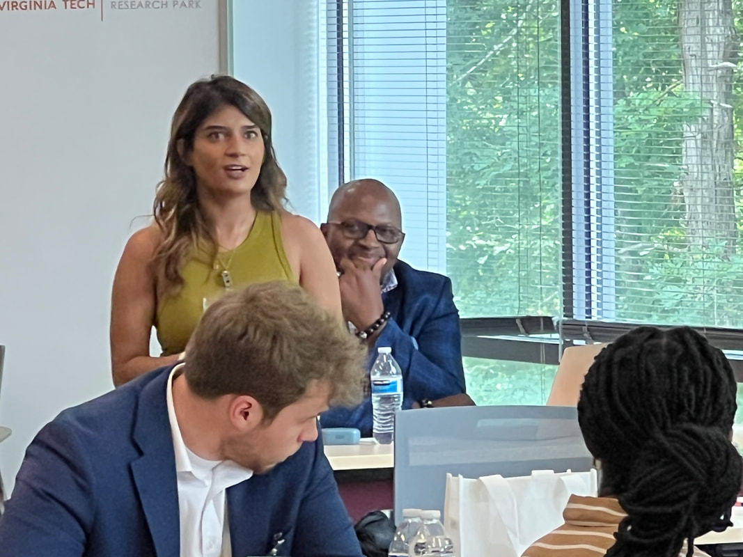 Participant in a sleeveless top speaking to seated teammates beside the windows