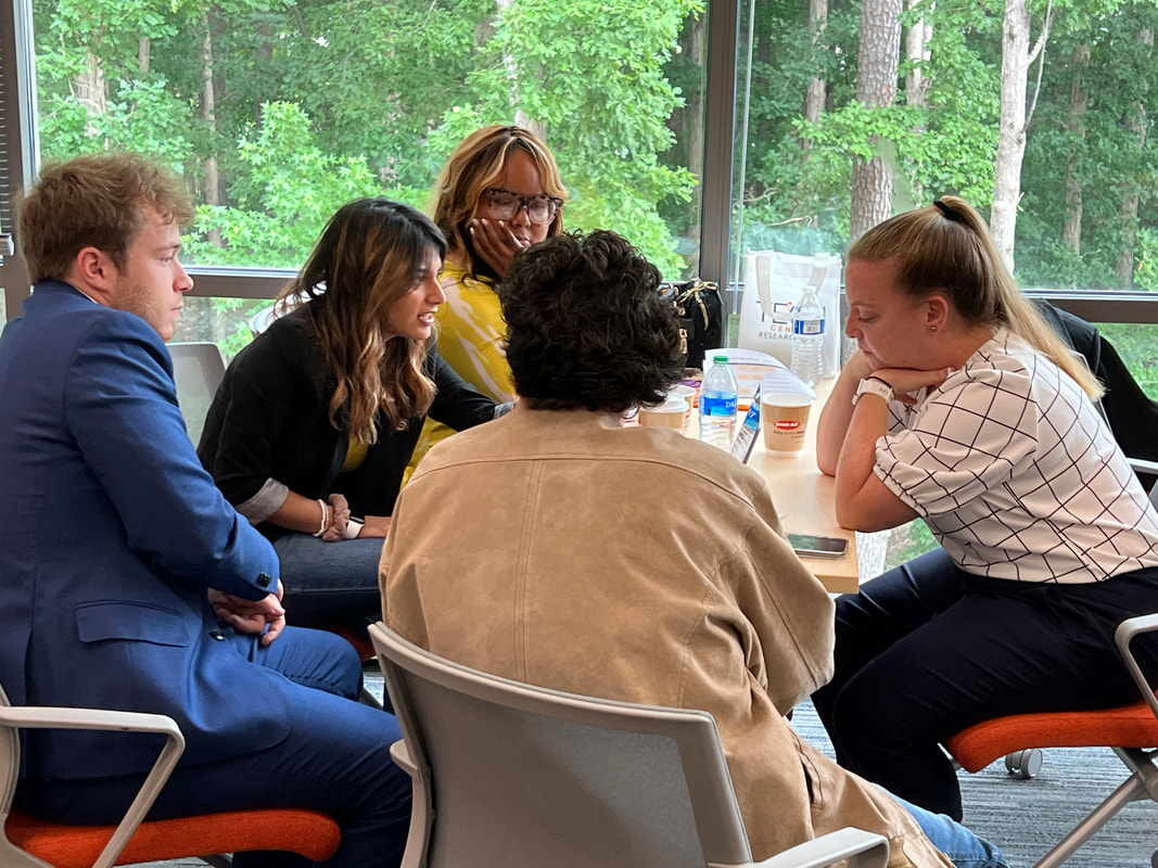 Five participants leaning in for a small-group discussion beside the windows