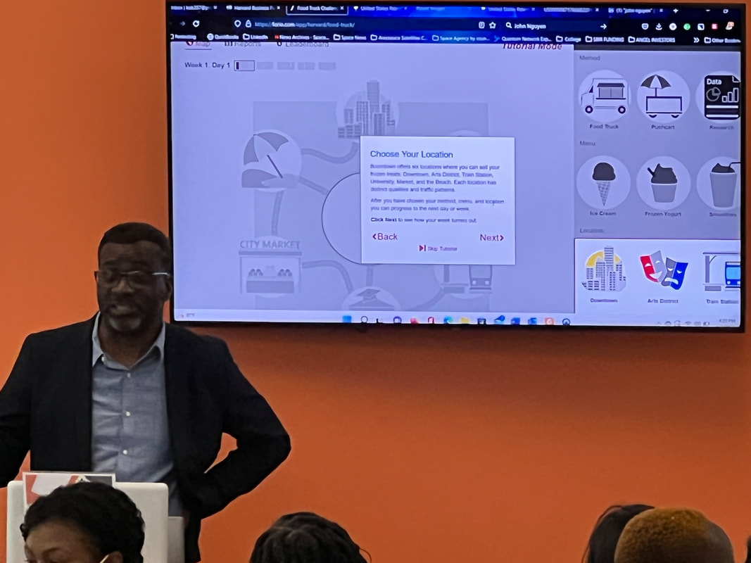 Presenter seated beside a projected technology slide in the workshop room