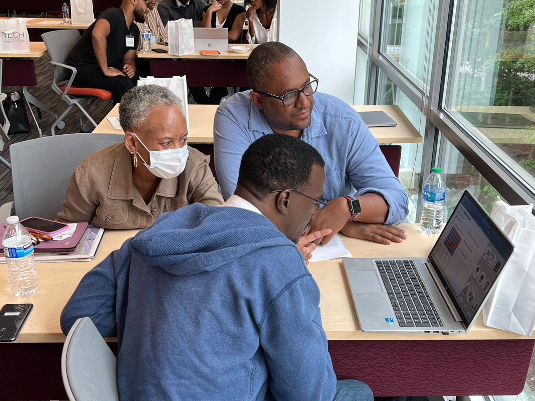 Four participants reviewing notes and a laptop beside the workshop room windows